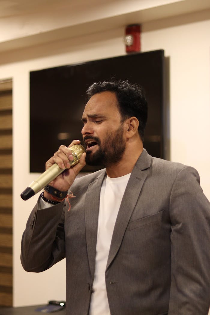A man in a suit sings passionately into a microphone at an indoor event.